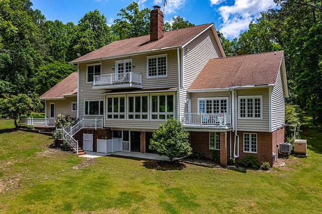 rear view of property with a sunroom, brick siding, a lawn, and a chimney