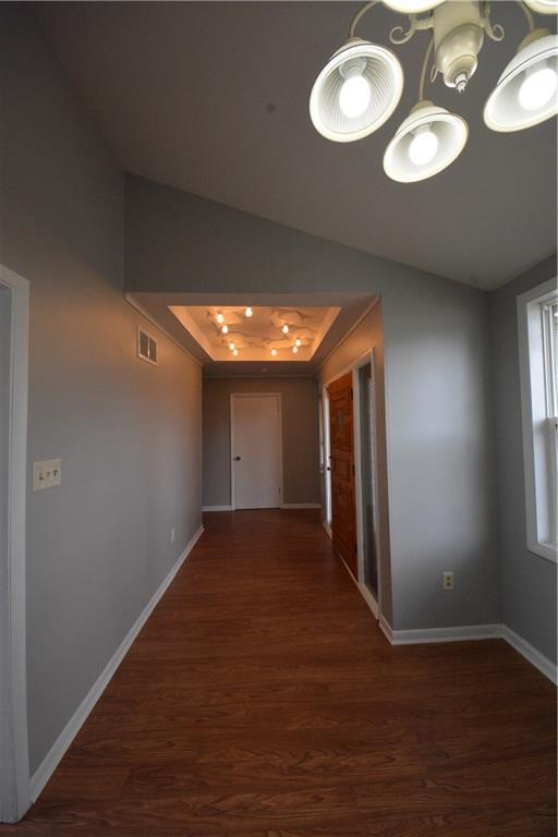 hall with a raised ceiling, dark wood-type flooring, and a chandelier