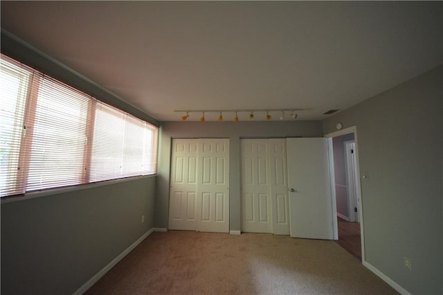 unfurnished bedroom with multiple windows, two closets, track lighting, and carpet flooring