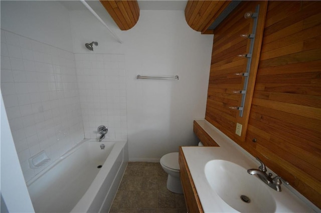 full bathroom with tiled shower / bath combo, toilet, wooden walls, tile flooring, and vanity