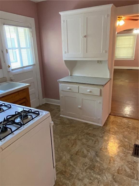 kitchen featuring white cabinets, gas range gas stove, sink, and dark tile flooring