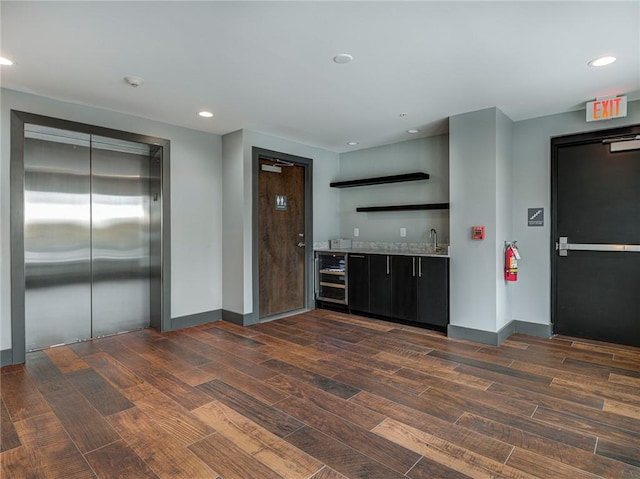 kitchen with sink, light stone counters, elevator, dark wood-type flooring, and wine cooler