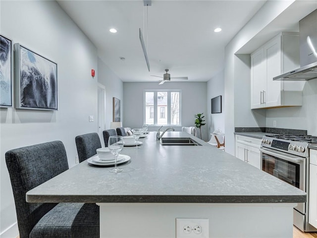 kitchen featuring sink, stainless steel range with gas cooktop, wall chimney exhaust hood, and an island with sink