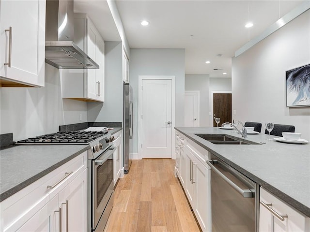 kitchen with appliances with stainless steel finishes, white cabinetry, light hardwood / wood-style flooring, wall chimney exhaust hood, and sink