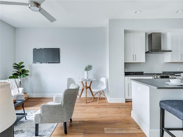 kitchen featuring wall chimney range hood, ceiling fan, range, light hardwood / wood-style floors, and white cabinetry