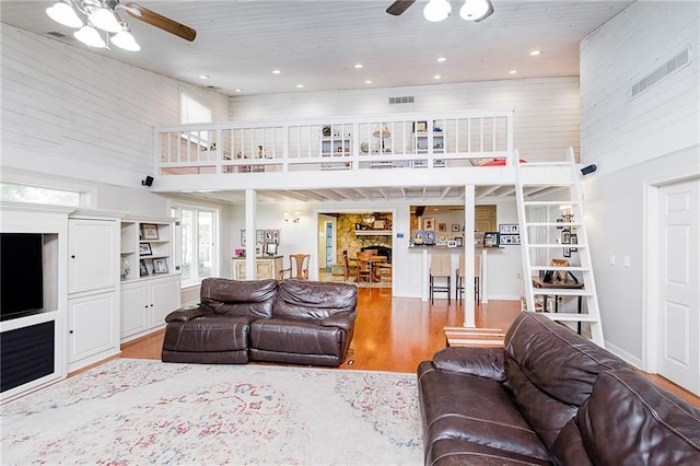 living room with ceiling fan, hardwood / wood-style flooring, wooden walls, and a high ceiling