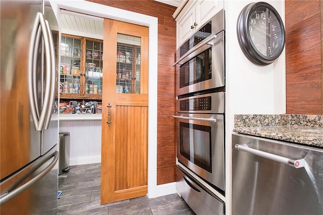 kitchen with white cabinets, wooden walls, stainless steel appliances, light stone countertops, and dark hardwood / wood-style flooring