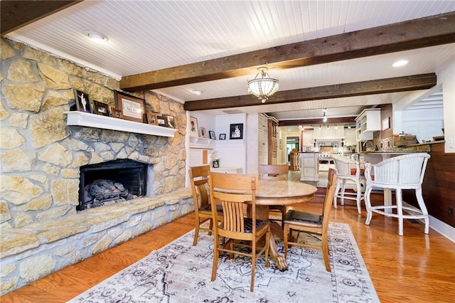 dining space featuring light wood-type flooring, a stone fireplace, and beam ceiling