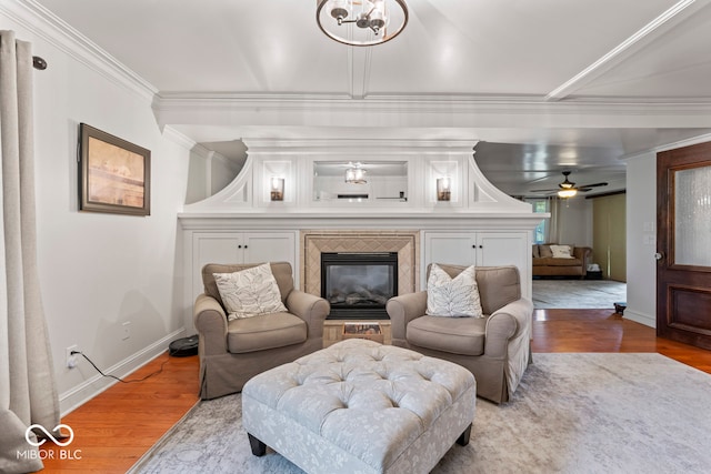 living room featuring ceiling fan with notable chandelier, a fireplace, crown molding, and light hardwood / wood-style flooring