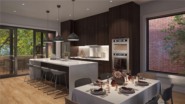 kitchen featuring decorative light fixtures, dark brown cabinetry, a center island with sink, stainless steel appliances, and light wood-type flooring