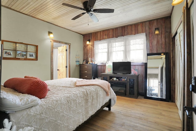 bedroom with wooden walls, ceiling fan, multiple windows, and light wood-type flooring