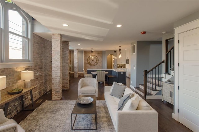 living room featuring a notable chandelier, brick wall, dark hardwood / wood-style floors, and decorative columns