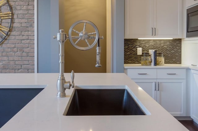 interior space featuring white cabinetry, backsplash, stainless steel microwave, sink, and dark hardwood / wood-style flooring