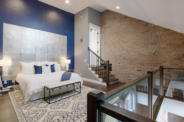 bedroom featuring a towering ceiling, brick wall, and hardwood / wood-style flooring