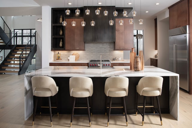 kitchen featuring stainless steel built in fridge, an island with sink, and decorative light fixtures