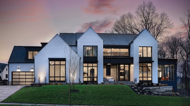 back house at dusk with a lawn and a garage