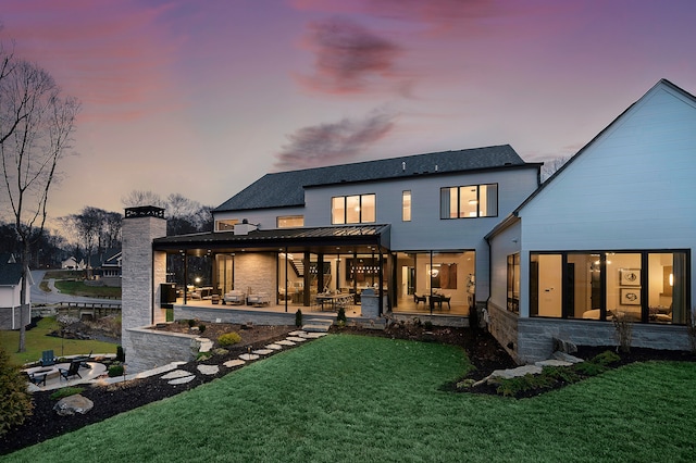 back house at dusk with a lawn and a patio area