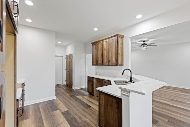 kitchen featuring light stone counters, ceiling fan, sink, dark wood-type flooring, and kitchen peninsula