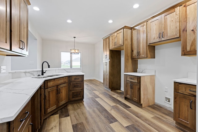 kitchen featuring sink, light stone countertops, light hardwood / wood-style flooring, pendant lighting, and an inviting chandelier