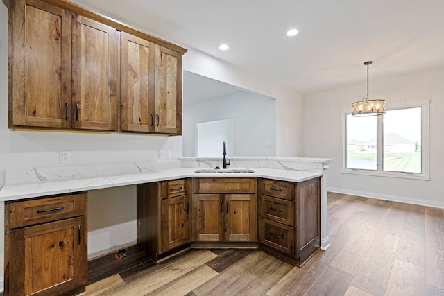 kitchen featuring light stone countertops, kitchen peninsula, wood-type flooring, sink, and pendant lighting