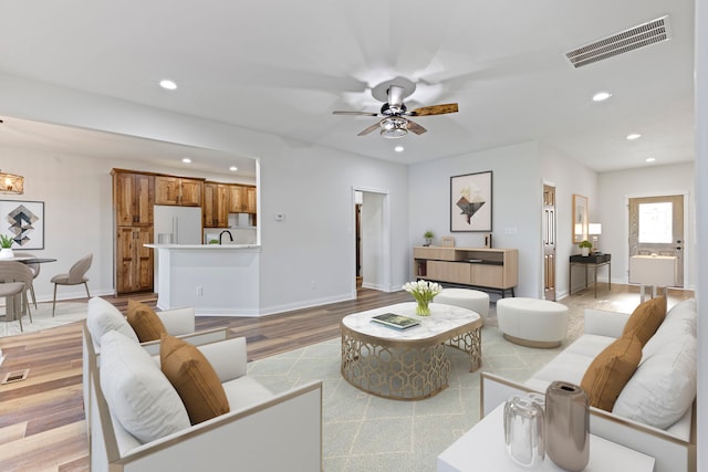 living room featuring ceiling fan, sink, and light wood-type flooring