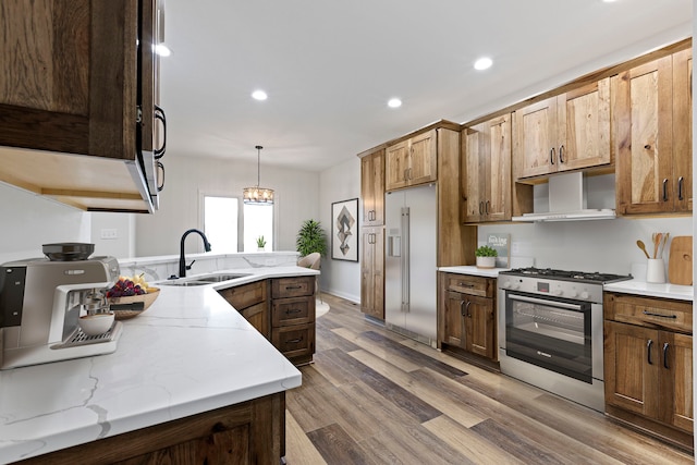 kitchen with appliances with stainless steel finishes, wall chimney exhaust hood, sink, hardwood / wood-style floors, and decorative light fixtures