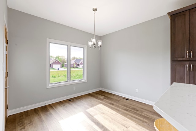 spare room with a notable chandelier and light wood-type flooring