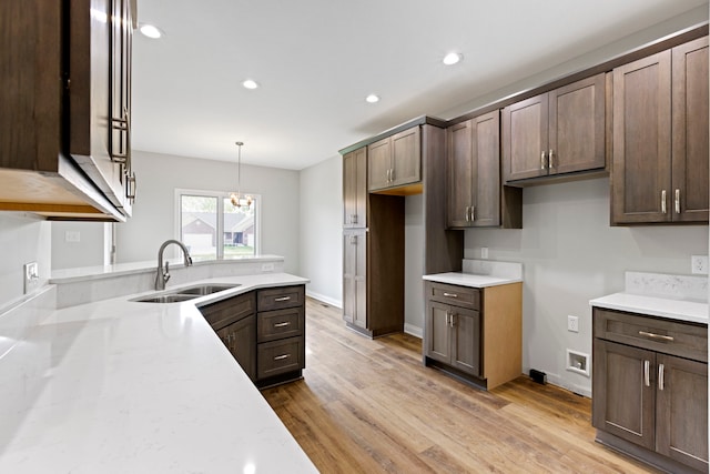 kitchen featuring light hardwood / wood-style floors, hanging light fixtures, sink, and light stone countertops