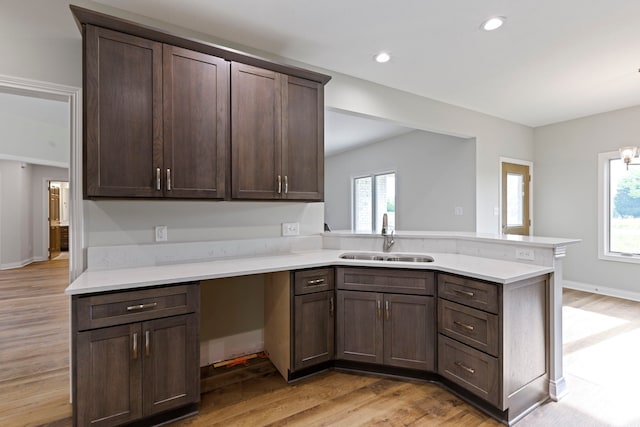 kitchen with dark brown cabinetry, sink, light hardwood / wood-style floors, and kitchen peninsula