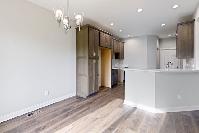 kitchen with decorative light fixtures, a chandelier, kitchen peninsula, sink, and hardwood / wood-style flooring