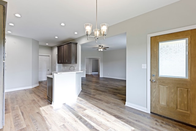 kitchen featuring ceiling fan with notable chandelier, pendant lighting, wood-type flooring, and dark brown cabinets