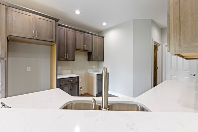 kitchen featuring dark brown cabinets, wood-type flooring, sink, and light stone countertops