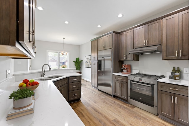 kitchen with sink, decorative light fixtures, stainless steel appliances, light hardwood / wood-style flooring, and light stone countertops