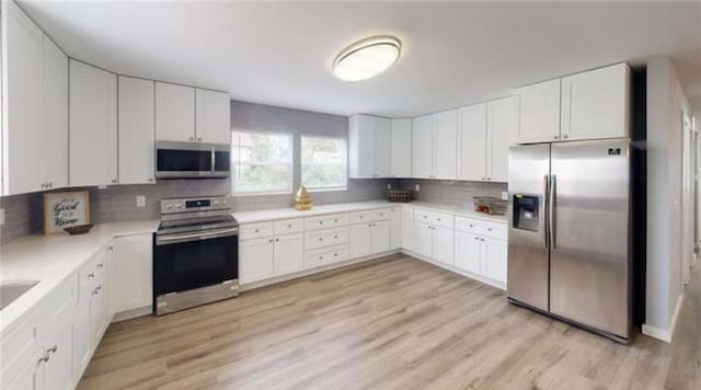 kitchen with white cabinets, appliances with stainless steel finishes, backsplash, and light wood-type flooring