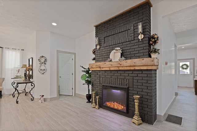 living room featuring brick wall, a fireplace, and light hardwood / wood-style flooring