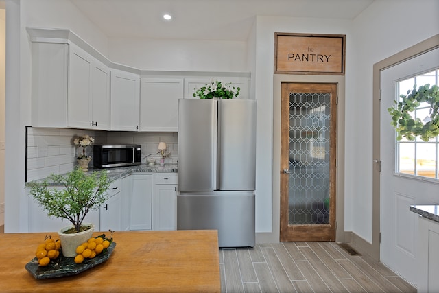 kitchen with light stone counters, light hardwood / wood-style flooring, backsplash, stainless steel appliances, and white cabinetry