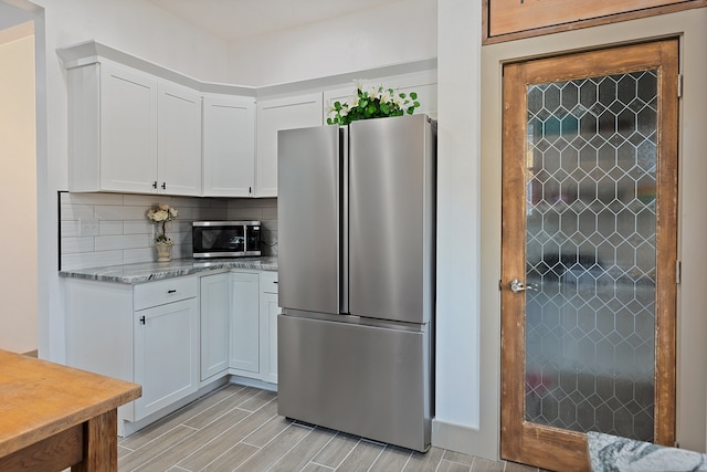 kitchen with white cabinets, appliances with stainless steel finishes, light stone counters, and tasteful backsplash