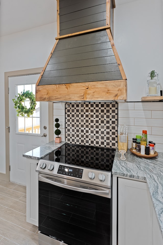 kitchen featuring light hardwood / wood-style floors, light stone countertops, stainless steel electric range, white cabinets, and backsplash