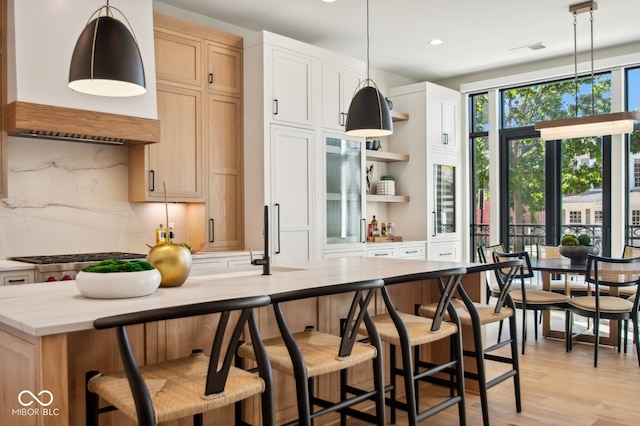 kitchen featuring hanging light fixtures, backsplash, stainless steel gas stovetop, and light hardwood / wood-style flooring