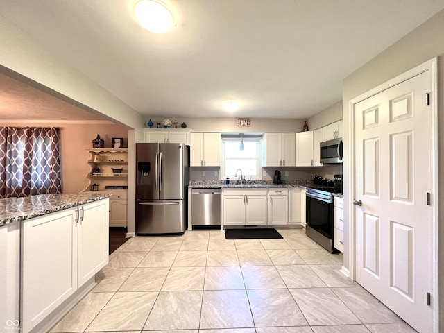 kitchen featuring dark stone counters, white cabinets, appliances with stainless steel finishes, and a sink