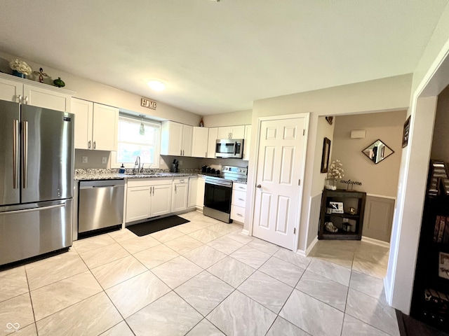 kitchen with light stone counters, wainscoting, a sink, stainless steel appliances, and white cabinetry