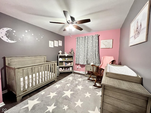 bedroom featuring a ceiling fan, baseboards, wood finished floors, and a nursery area