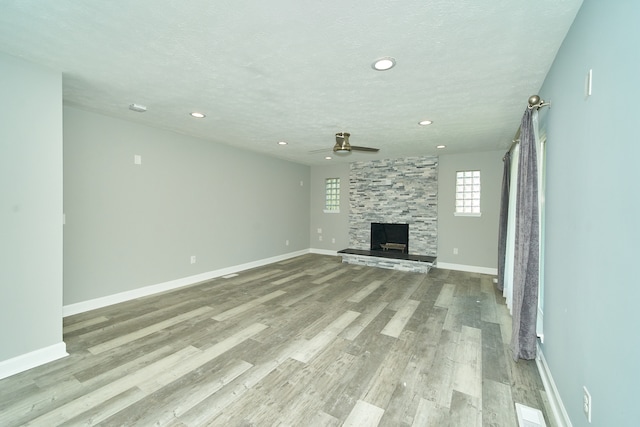 unfurnished living room with light hardwood / wood-style floors, a textured ceiling, a fireplace, and ceiling fan