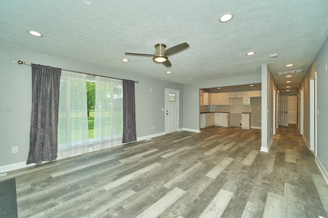 unfurnished living room featuring ceiling fan, dark wood-type flooring, and a textured ceiling