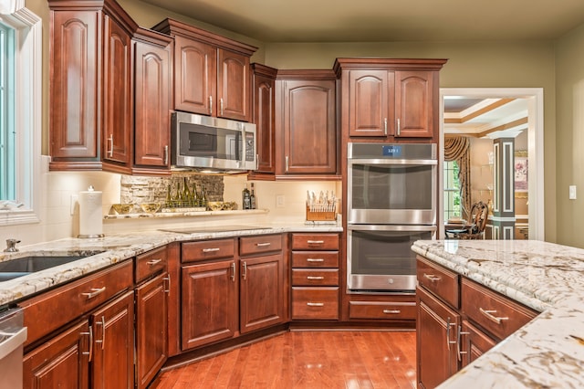 kitchen with wood-type flooring, a raised ceiling, light stone counters, and stainless steel appliances