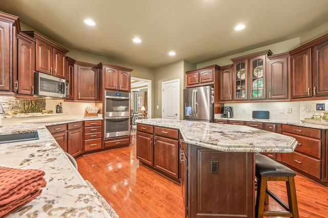 kitchen featuring backsplash, appliances with stainless steel finishes, a kitchen bar, light wood-type flooring, and a center island