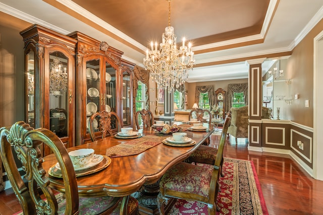 dining space featuring an inviting chandelier, decorative columns, a raised ceiling, dark hardwood / wood-style flooring, and ornamental molding