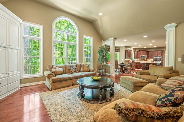 living room with decorative columns, light wood-type flooring, and vaulted ceiling