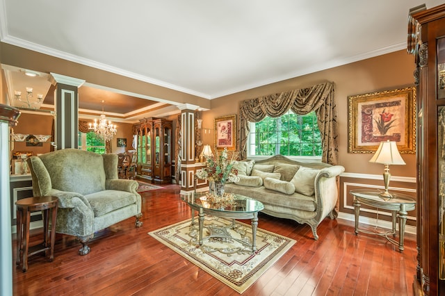 living room with crown molding, dark wood-type flooring, ornate columns, and a chandelier