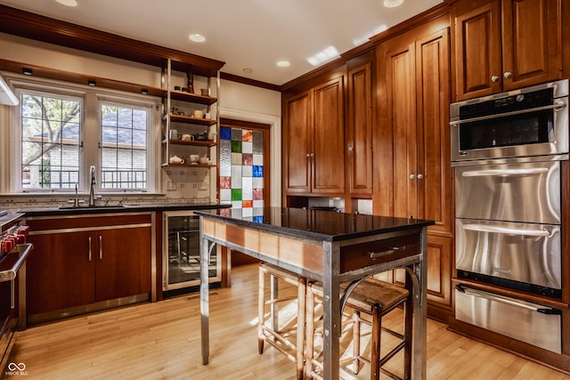 kitchen with dark stone counters, stainless steel appliances, crown molding, sink, and light hardwood / wood-style floors